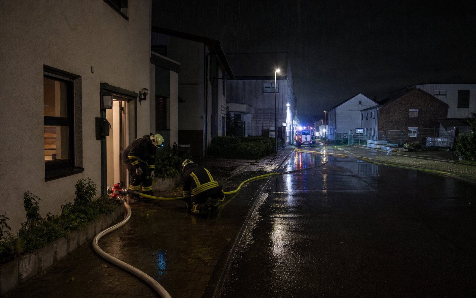 Feuerwehrleute pumpen bei Starkregen Wasser aus einem Keller