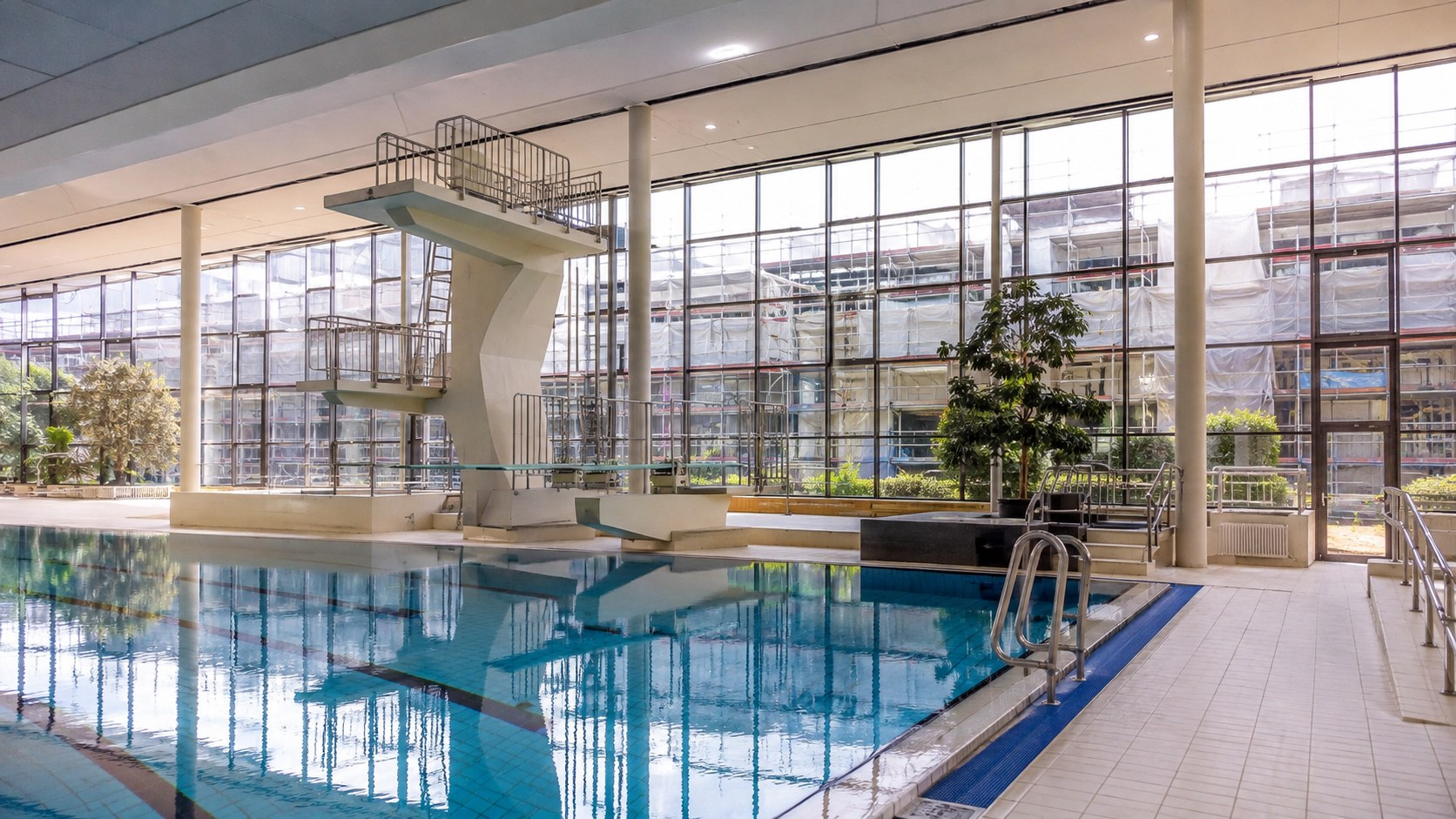 Innenansicht eines kommunalen Hallenbads mit Schwimmbecken und Sprungturm