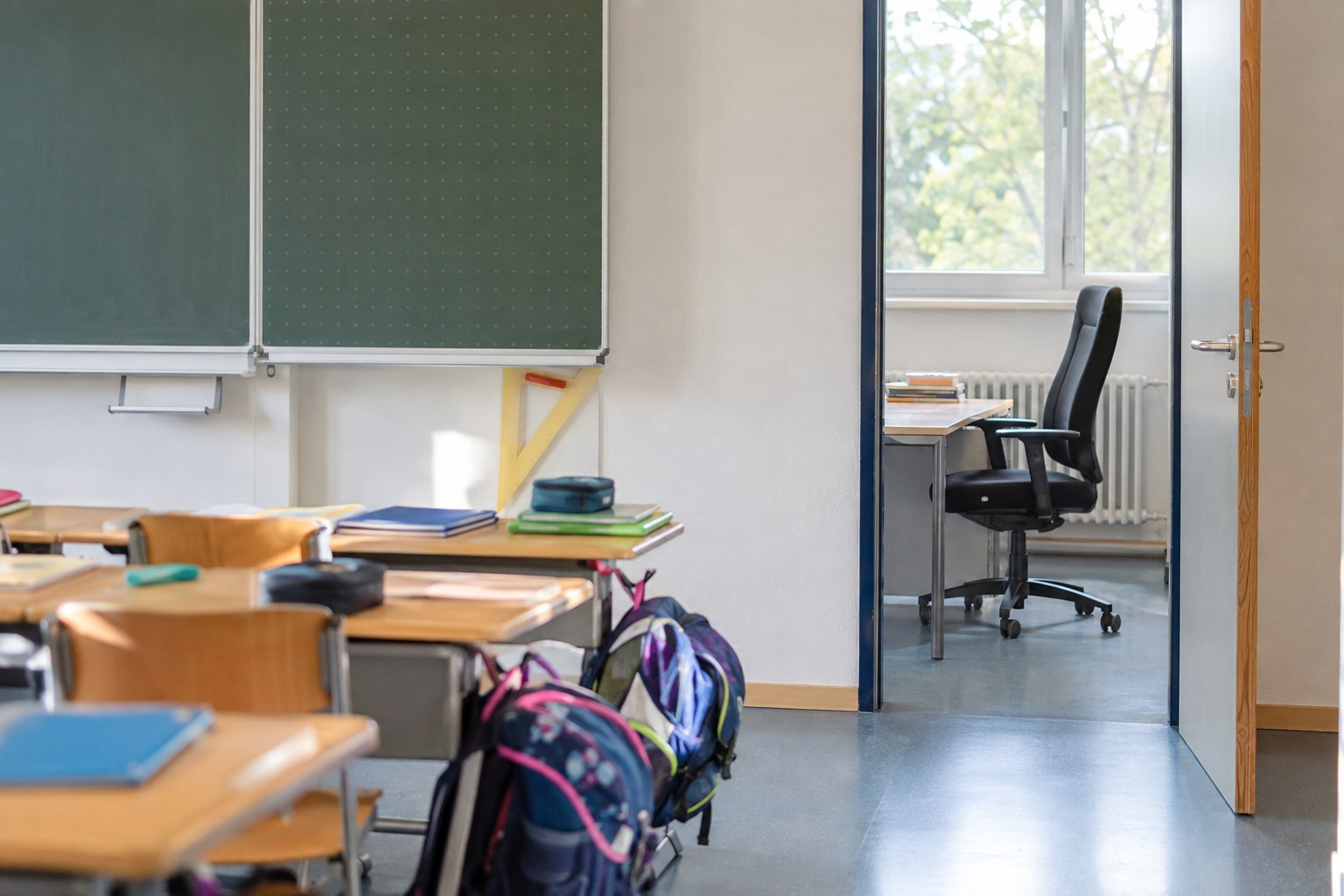Leeres Klassenzimmer mit Schultaschen und Blick auf einen unbesetzten Bürostuhl